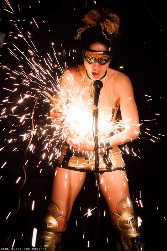 angle grinding performance artist sings while making sparks fly off of her torso in a live performance on stage