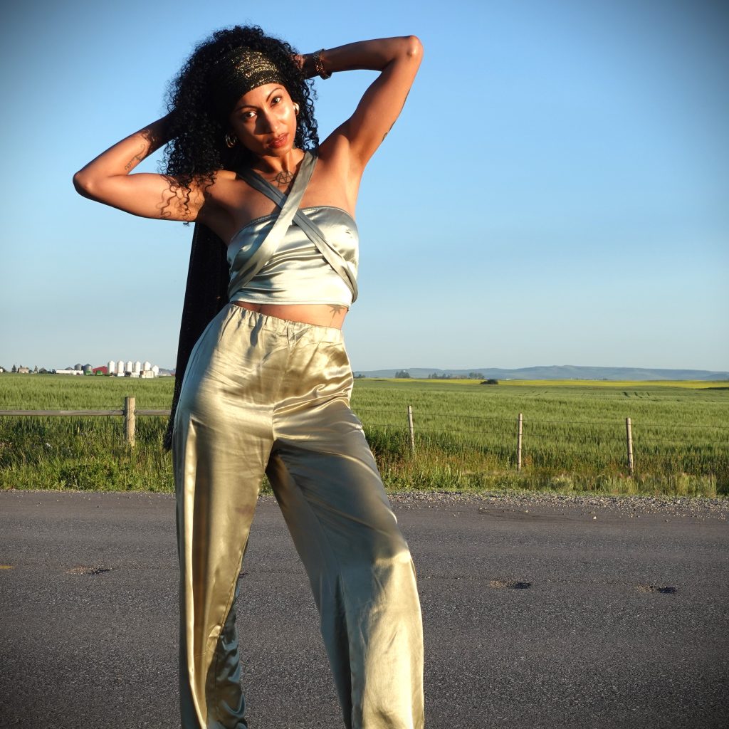 tattooed fashion model wearing an emerald green satin two piece pant suit poses on a highway surrounded by farmland