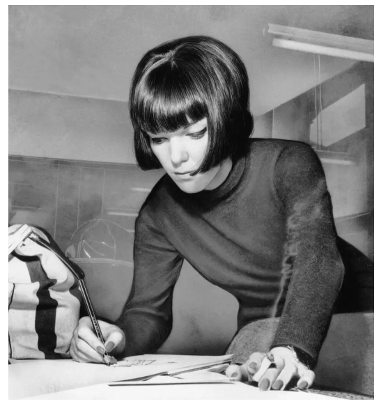A woman in a black sweater, Mary Quant, writing on a piece of paper, showcasing her creativity