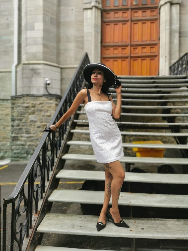 On a set of steps, a woman exudes elegance in a white dress and hat, reminiscent of Audrey Hepburn's iconic style.
