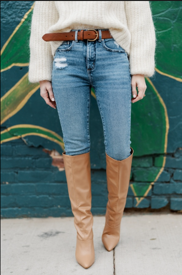 Woman in thigh high brown boots wearing white neutral sweater and jeans