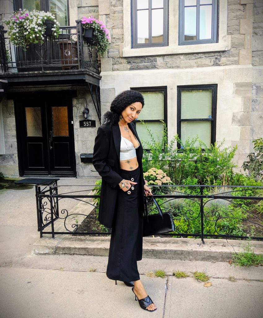 Fashionable woman in black blazer, bra top, and pants strolling along the street.