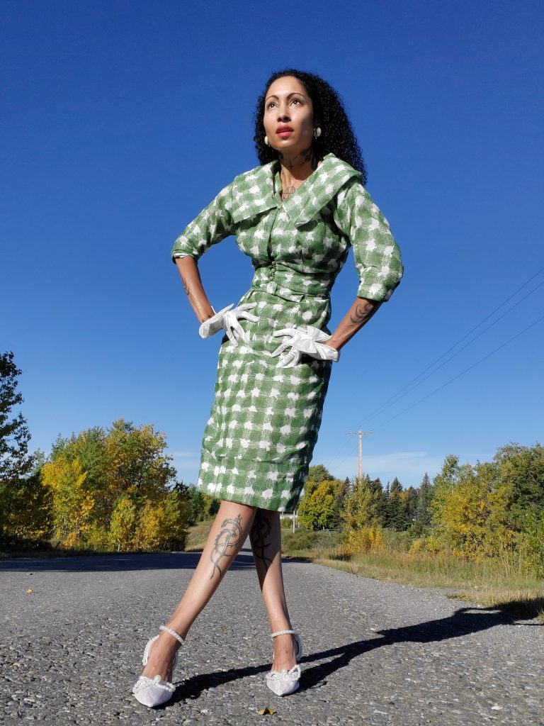 Adorned in a meticulously tailored 2-piece dress and jacket, this woman radiates elegance. The green and white checkered pattern adds a touch of vintage charm to her impeccable style.