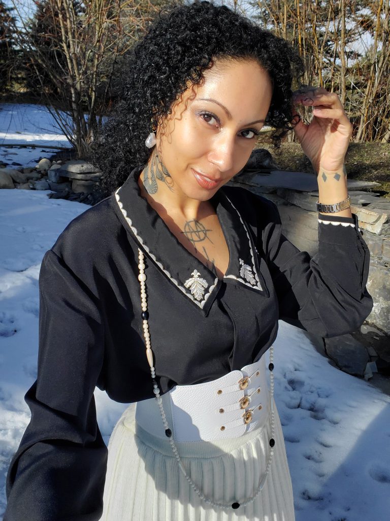 Elegant woman in white skirt striking a pose in the snow, wearing 1970s vintage pleated skirt, embroidered blouse, pearl jewelry.