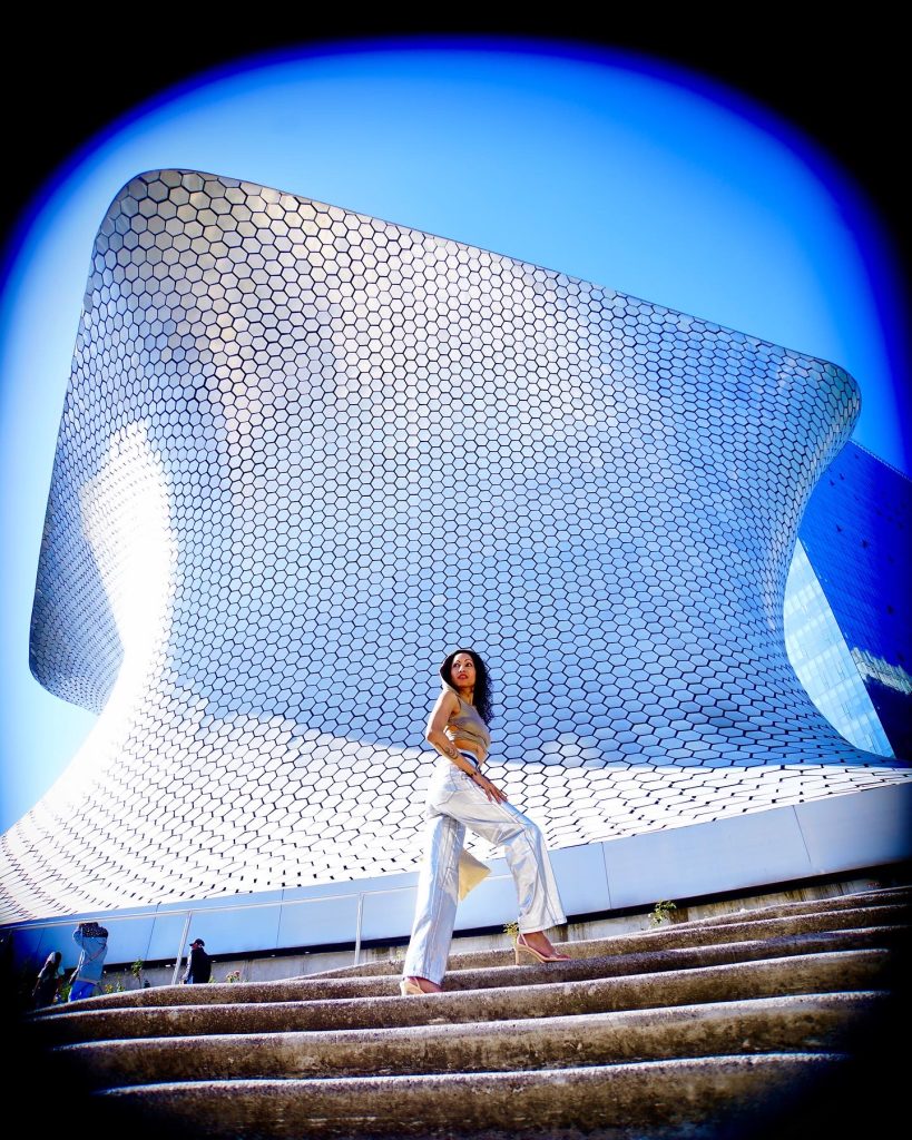 A stylish lady, clad in shimmering silver pants, elegantly poses against the backdrop of a grand museum.