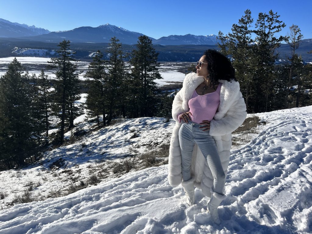 Elegant woman in pink sweater and white fur coat standing on snowy mountain