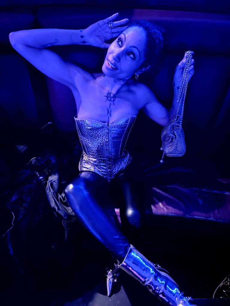 A captivating lady, adorned in a corset and leather pants, exudes elegance as she gracefully rests upon a lavish couch.