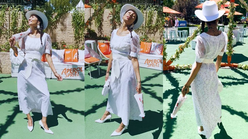 A woman in a pristine white 1970s vintage dress and fashionable hat poses gracefully, embodying timeless elegance and poise for the photograph.