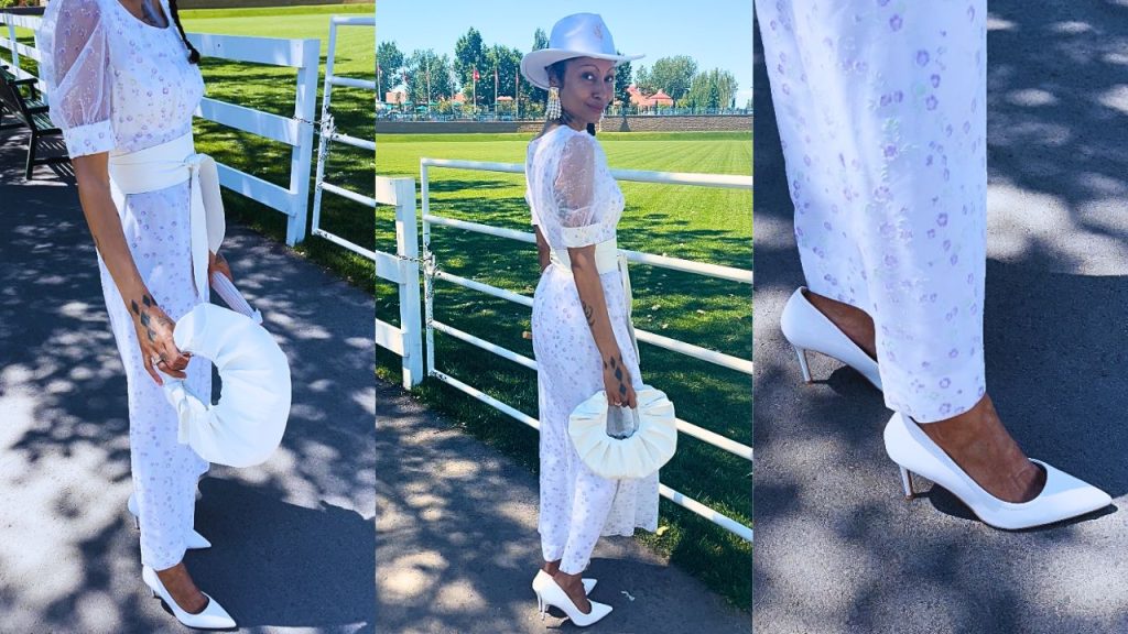 Captivating in a white floral dress and stylish hat, a woman strikes a pose, radiating elegance and charm at an equistrian horse jumping event at Spruce Meadows